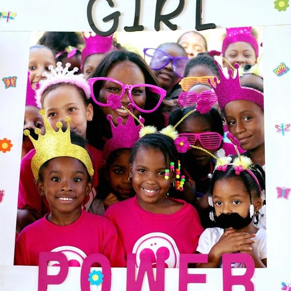 A joyful group of girls and a woman celebrating girl power with colorful crowns and glasses.