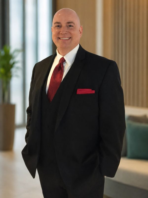 Man in a black suit with a red tie and pocket square smiling.
