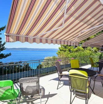 A sunny patio with colorful chairs and a striped awning overlooking the sea.