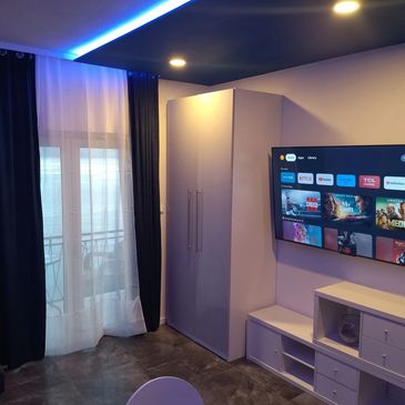 Modern living room with TV, wardrobe, and blue LED ceiling lights.