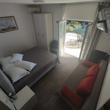 Cozy bedroom with bed, sofa, and balcony overlooking outdoor seating area.