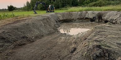 Excavator digging a large hole in a field.