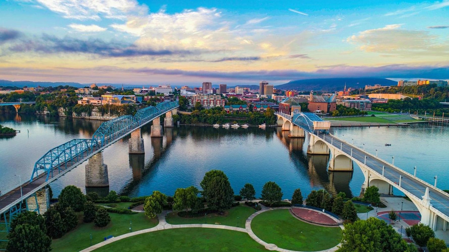Two bridges spanning a river with a cityscape and mountains in the background.
