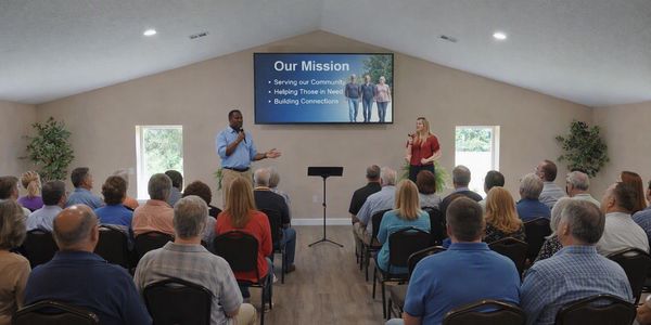 Two presenters sharing a community mission in a meeting room.