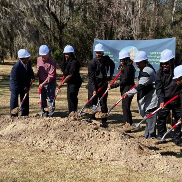 Group of people in hard hats breaking ground with shovels.