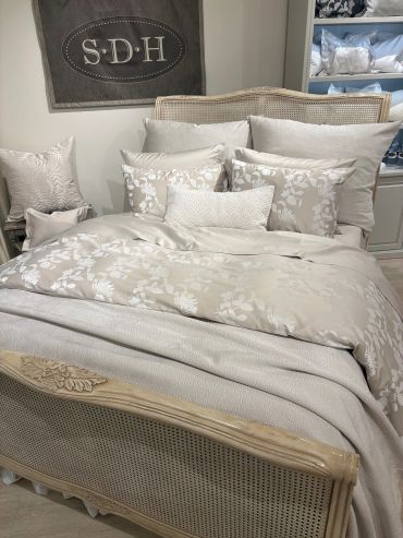 Elegant bed with beige floral bedding and multiple pillows in a cozy bedroom.