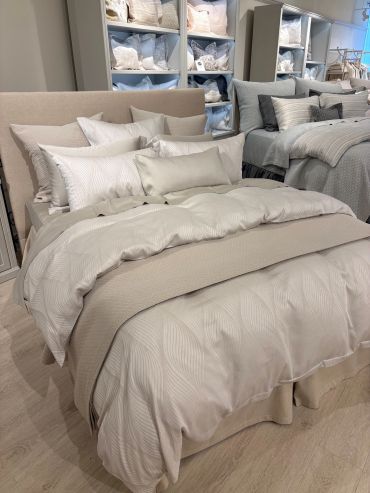 Luxurious beige and white bedding set on a plush bed in a showroom.