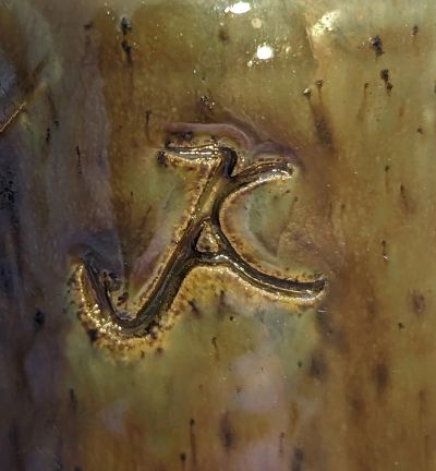 A close-up of a carved or branded letter 'K' on a yellowish surface.