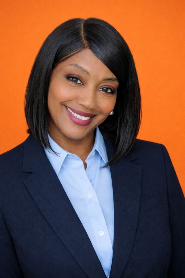 Confident woman in business attire smiling against an orange background.