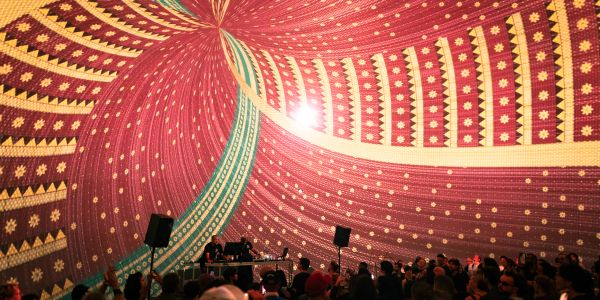 Large crowd under a colorful tent with a DJ playing music.