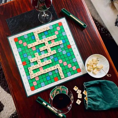 Scrabble game on a table with wine and cheese.