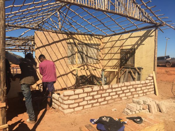 Two men working on a partially built brick structure under a bamboo roof frame.