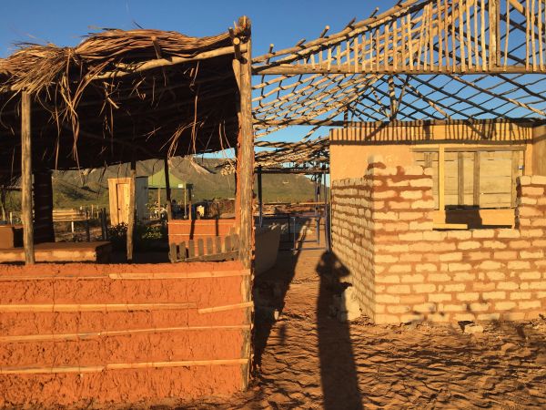 Partially built mud brick houses with wooden roofs in a rural setting at sunset.