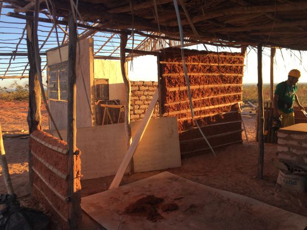 Construction of a rustic building using adobe and wooden materials at sunset.