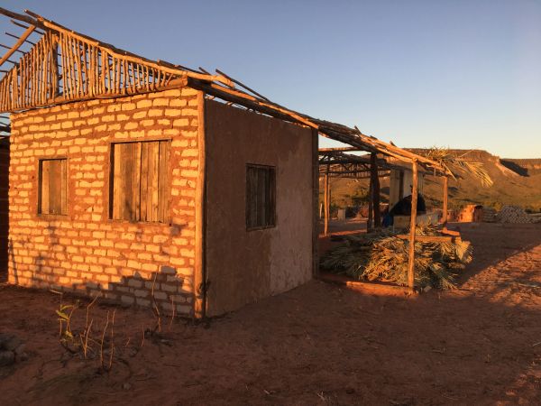 A rustic, unfinished brick house in a dry, sunlit landscape.