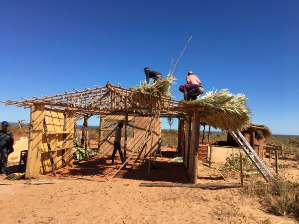 People constructing a thatched roof on a wooden frame under a clear blue sky.