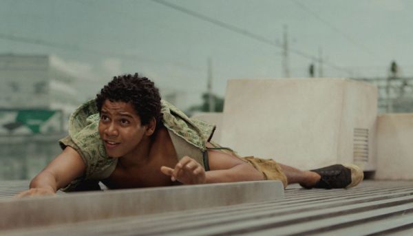 Young man lying on rooftop, looking intrigued and cautious.