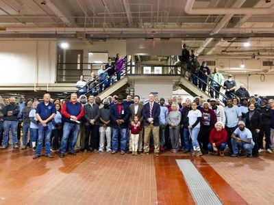 Large group of diverse people posing indoors in front of stairs.