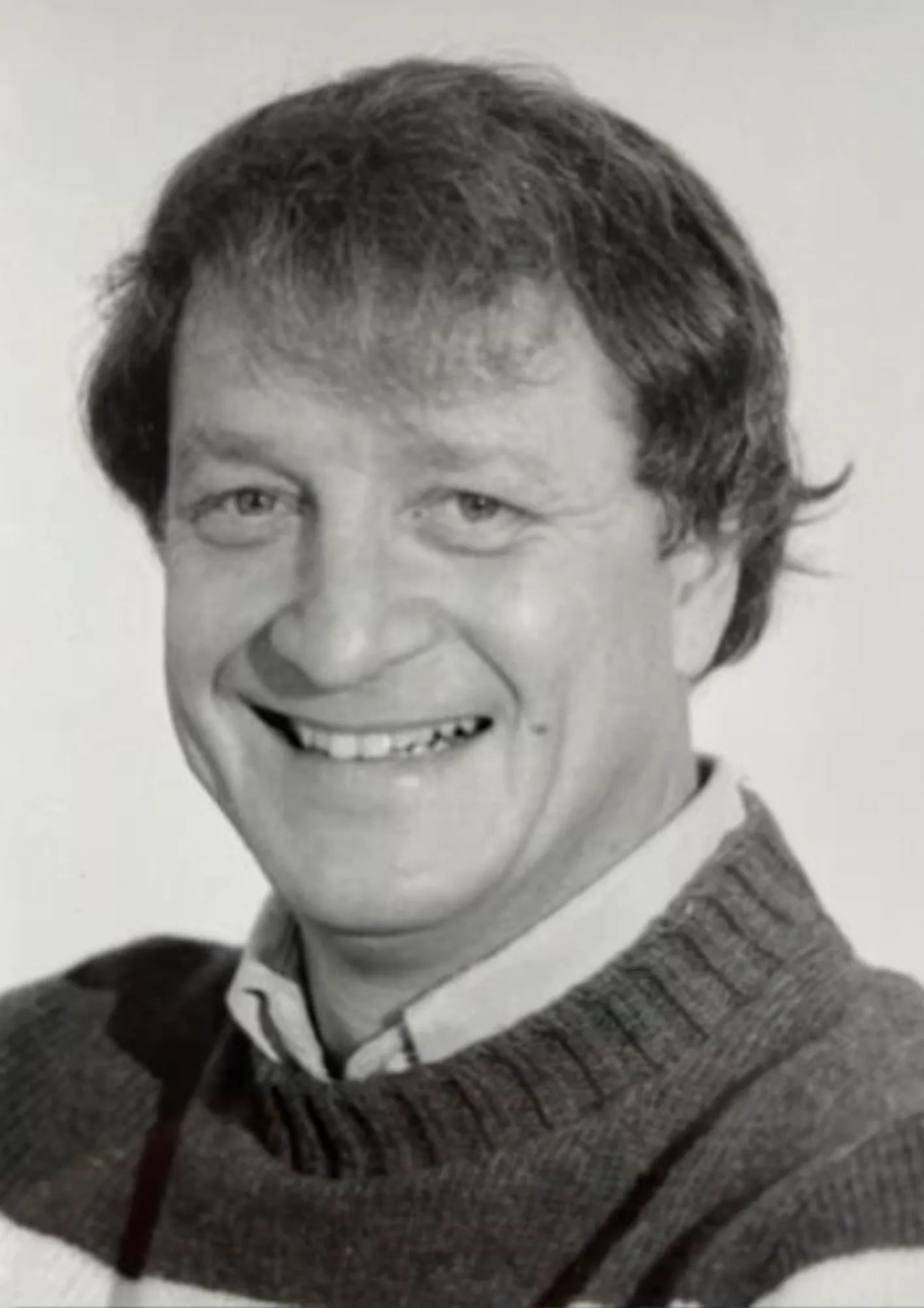Black and white portrait of a smiling man in a knitted sweater.