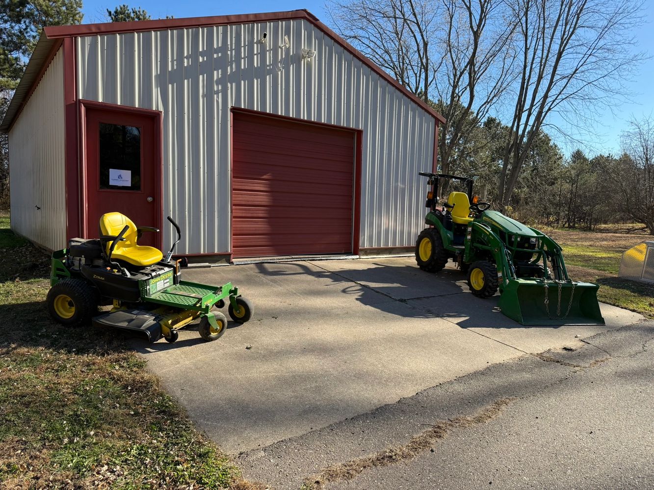 Two John Deere lawn machines parked outside a metal garage.