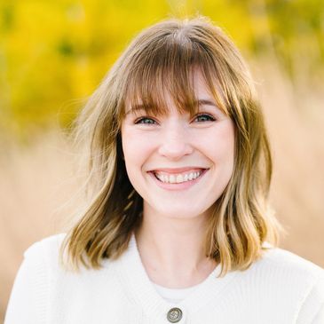 Young woman with shoulder-length hair smiling brightly in a white sweater.