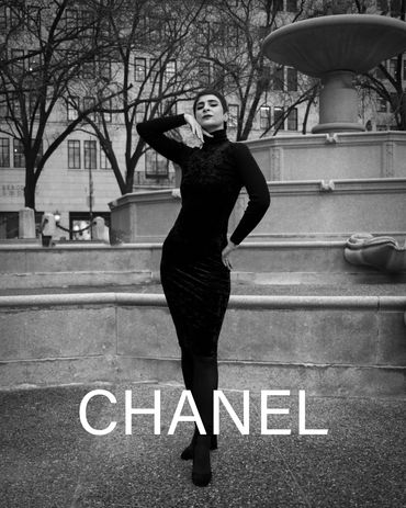 Woman in a black dress posing by a fountain with CHANEL text.