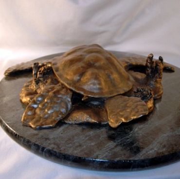 Bronze turtle sculpture resting on a dark stone base.