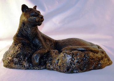 A bronze sculpture of a reclining panther on a textured base.