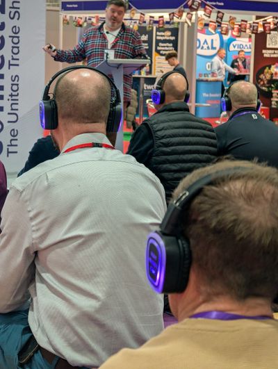 Audience with headphones listening to a speaker at a trade show.