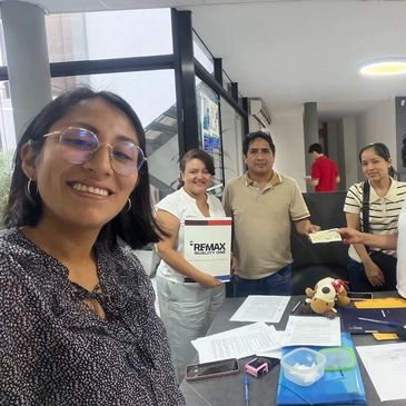 Four people smiling and holding a RE/MAX Realty certificate indoors.