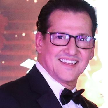 Man in tuxedo and glasses smiling at an event.