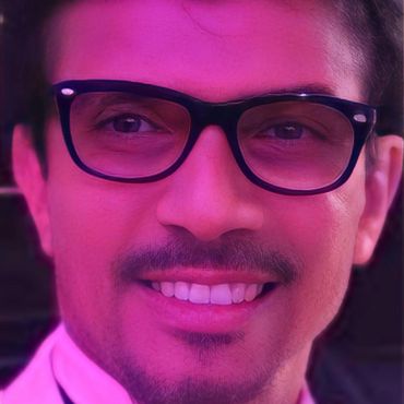 Close-up of a smiling man wearing black glasses with a pinkish-purple light effect.