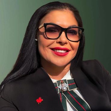 Smiling woman with glasses and a red lipstick, wearing a black blazer with a maple leaf pin.