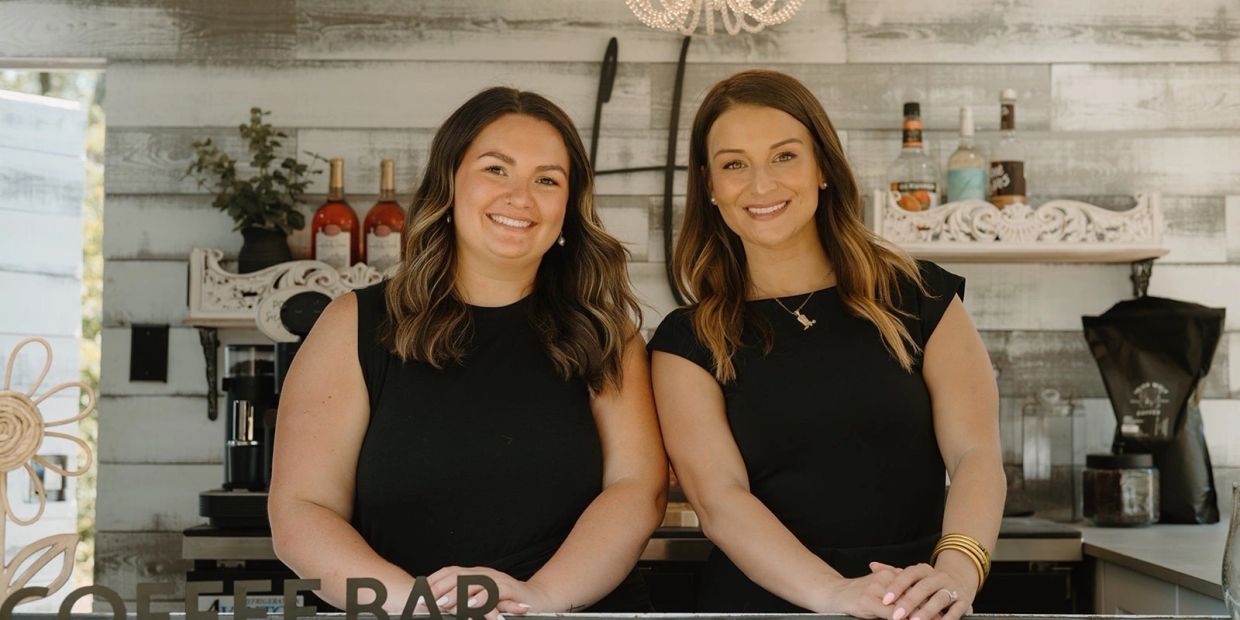 Two women smiling behind a coffee bar counter.