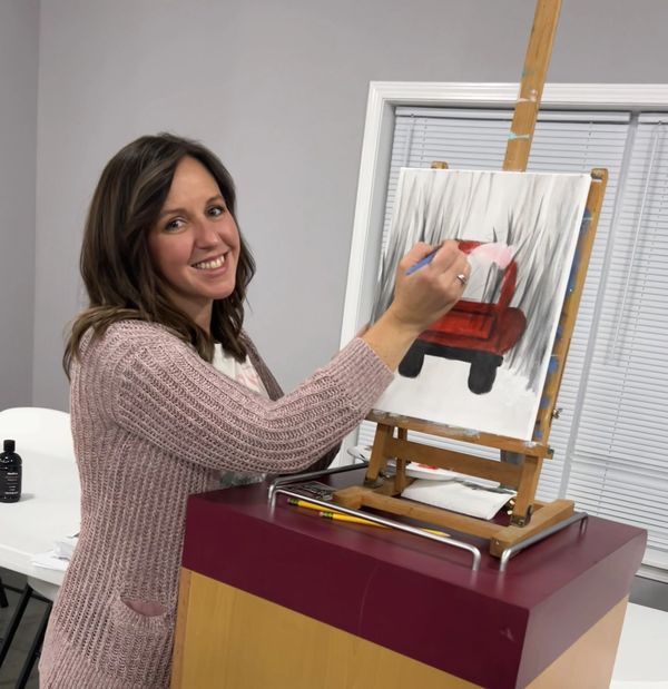 Woman painting a red tractor on canvas.