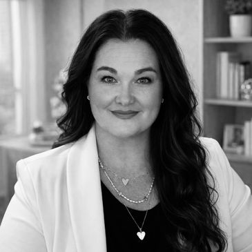 Confident woman with long dark hair wearing a white blazer and layered heart necklaces.