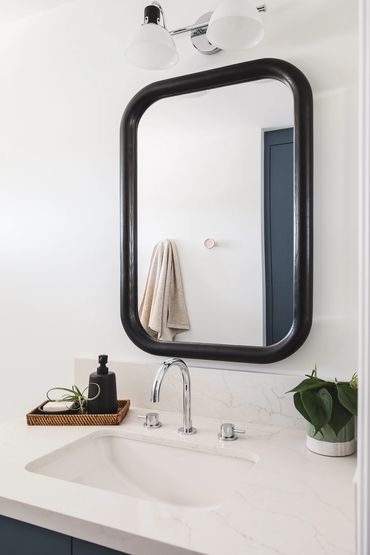 close up of a bathroom vanity  with white countertop, black framed mirror, chrome faucet & soap tray
