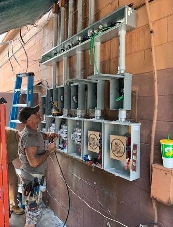 Electrician working on multiple electrical panels mounted on a wall.