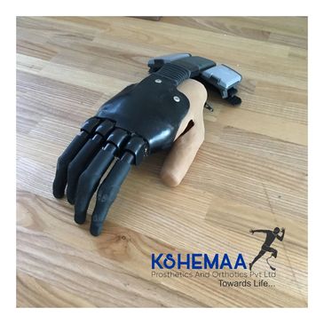 Advanced prosthetic hand with flexible black fingers and a beige thumb on a wooden surface.
