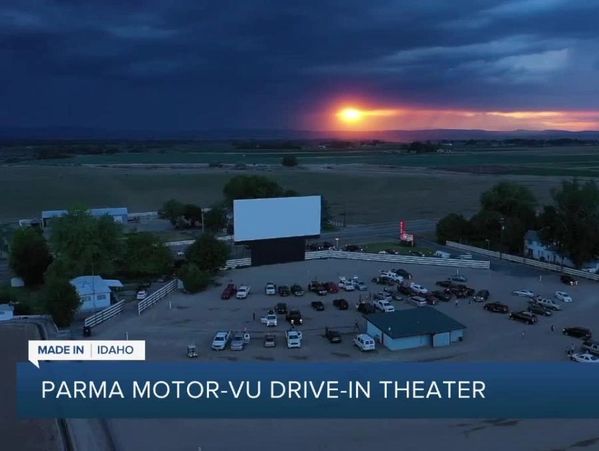 Drive-in theater at sunset with cars parked facing a large screen.