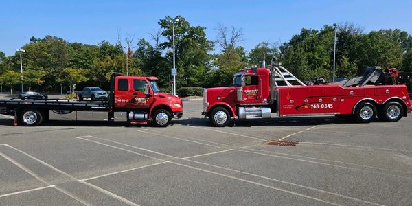 Two red tow trucks parked facing each other in an empty lot under a clear blue sky.