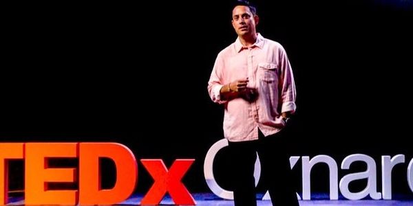 Man delivering a TEDx talk on a red circular carpet under bright stage lights.
