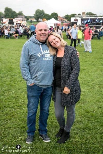 A couple smiling and posing together at an outdoor event on a grassy field.