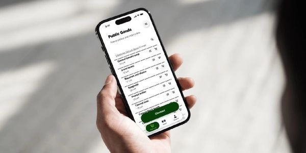Hand holding smartphone displaying a shopping list on a public goods app.