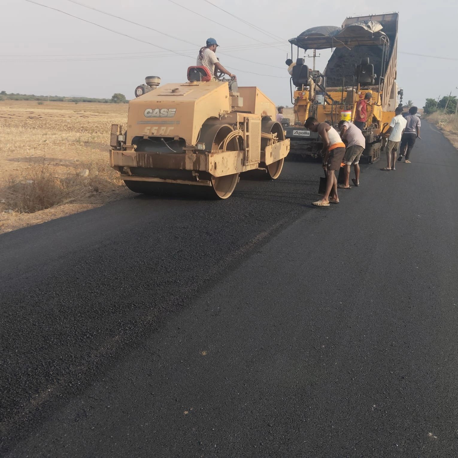 Construction workers paving a rural road with heavy machinery.
