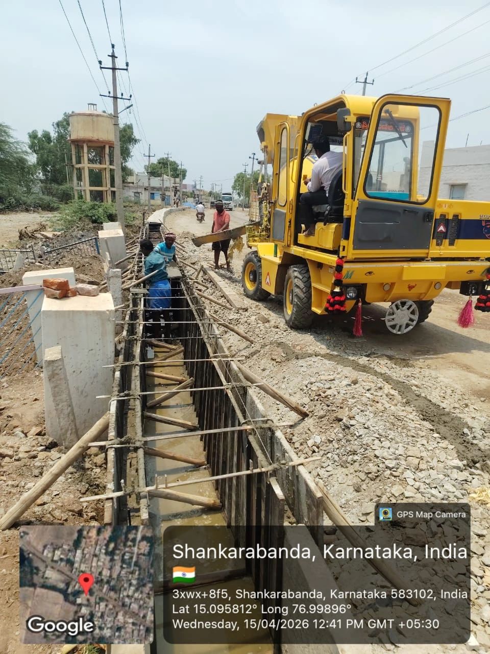 Workers pouring concrete into a trench using a yellow construction machine in Shankarabanda, Karnataka.