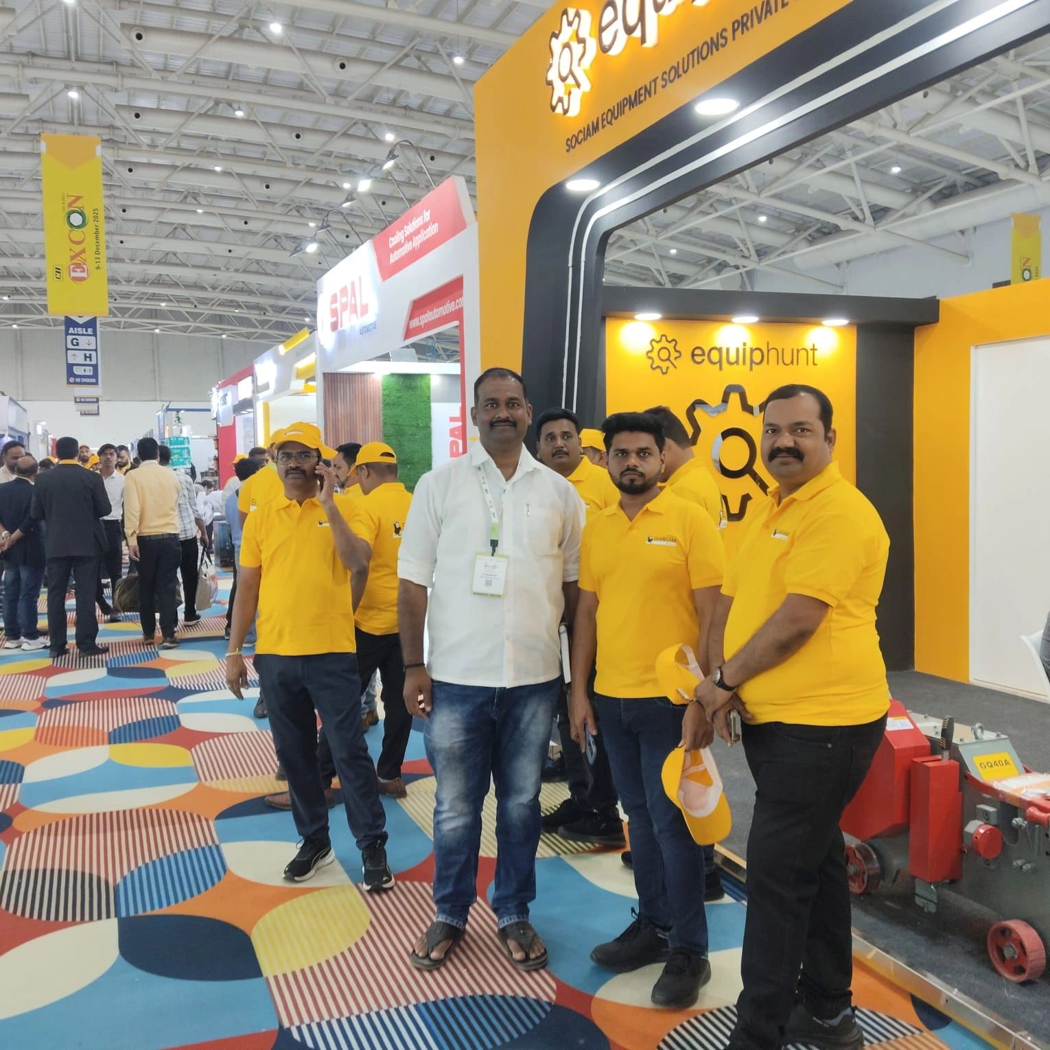 Group of men at a trade show booth wearing yellow shirts and caps.