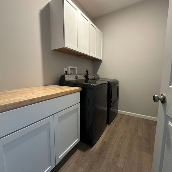 Modern laundry room with black washer and dryer, white cabinets, and wooden countertop.