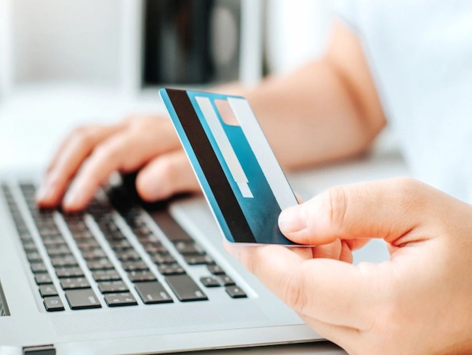 Person holding credit card near a laptop keyboard.