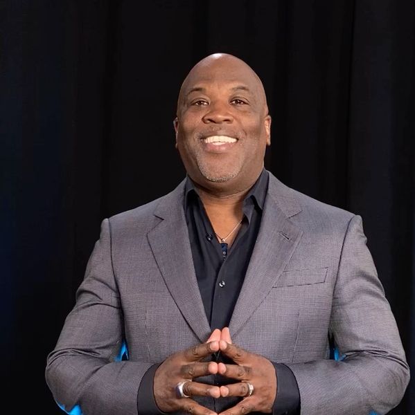 Smiling man in suit with hands clasped.